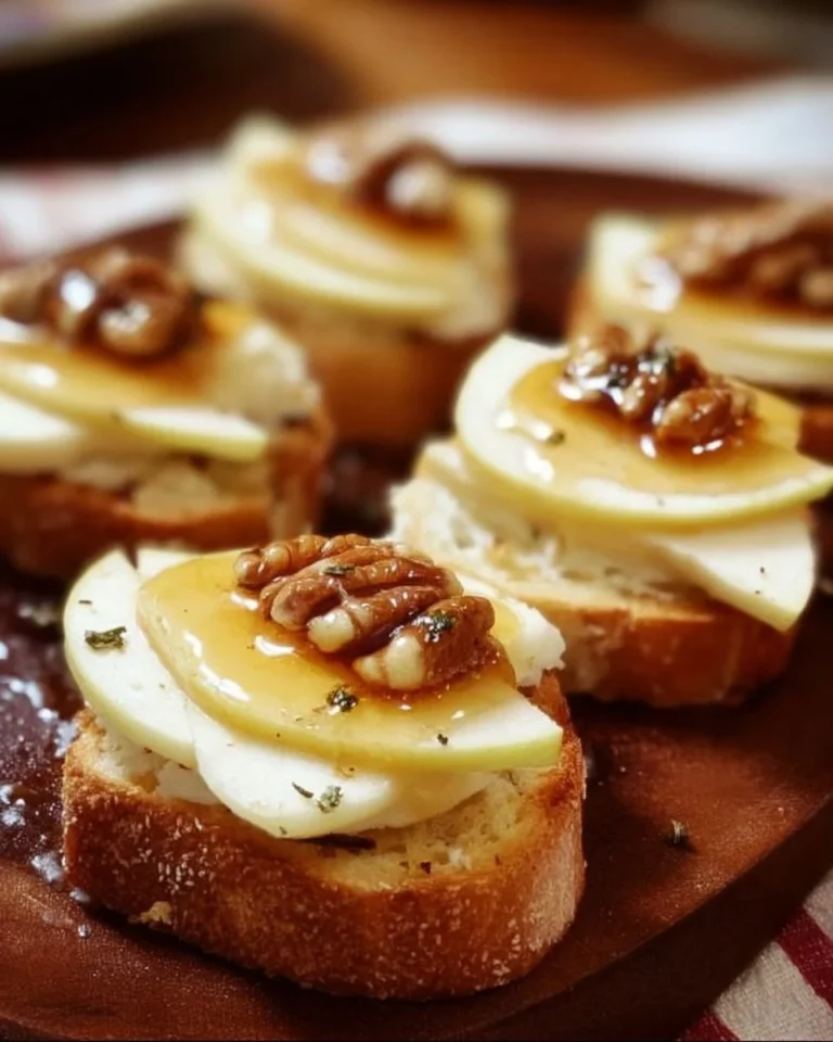 Brie crostini topped with apple slices and drizzled with honey on a wooden platter