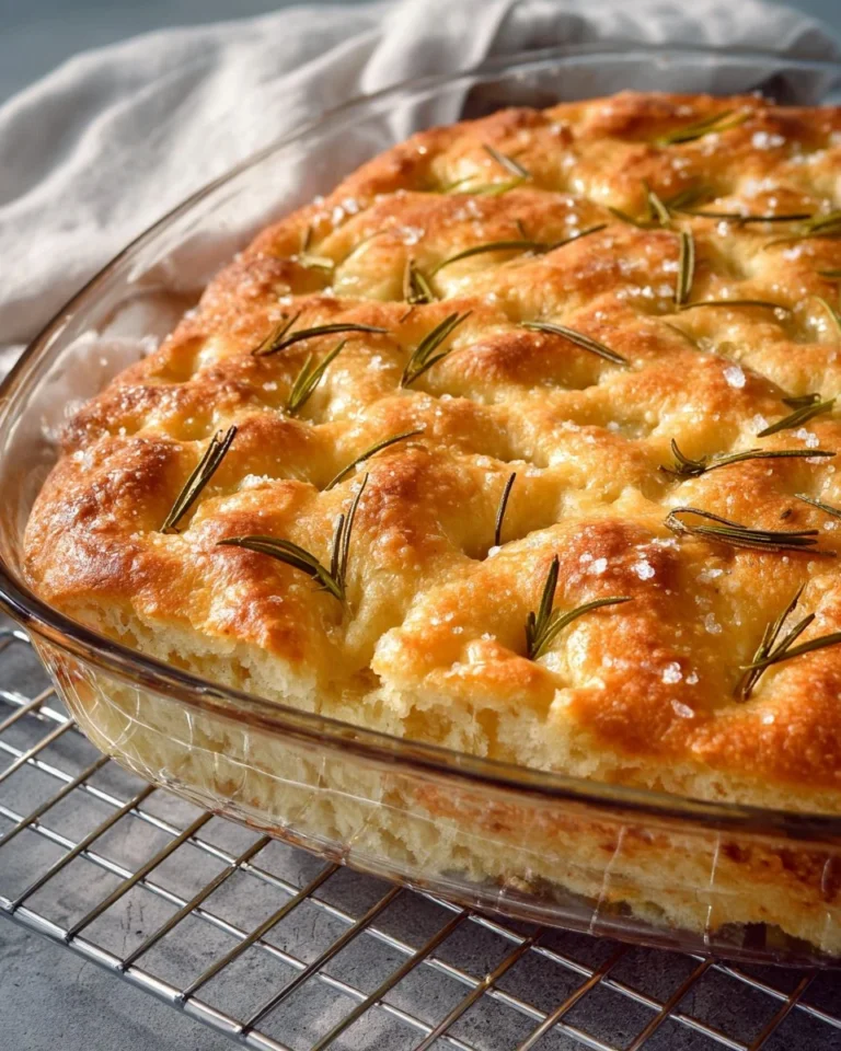 Homemade rosemary focaccia bread with herbs and olive oil on a wooden board.
